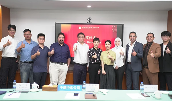 An international group of ten business professionals, representing both CSCEC Middle East and industrial adhesive manufacturer INGADA, gives a unified 'thumbs-up' gesture in a professional conference room. They are standing in front of a large presentation screen displaying 'Award Ceremony' in Chinese and English. This photo commemorates the successful technical alignment and supply chain partnership for extreme-climate construction projects.